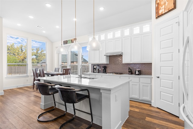 kitchen with sink, hanging light fixtures, white cabinets, hardwood / wood-style flooring, and a kitchen island with sink