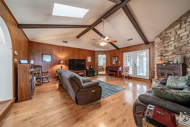 living room with wood walls, beamed ceiling, light hardwood / wood-style flooring, a fireplace, and a skylight