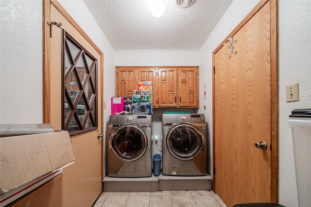 laundry room featuring light tile patterned floors, a textured ceiling, cabinets, and washer and clothes dryer