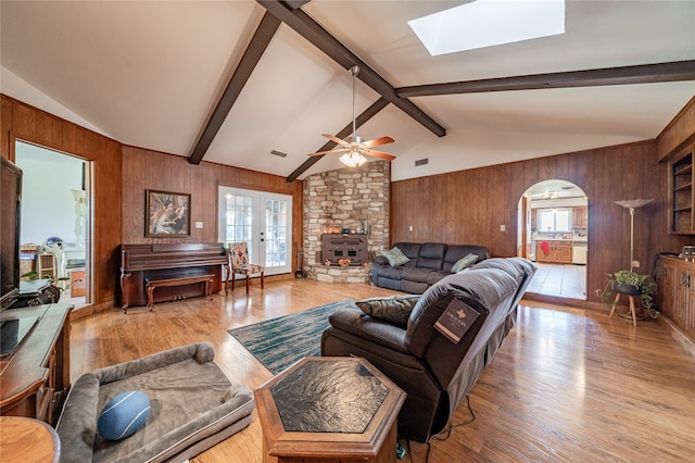 living room with wooden walls, vaulted ceiling with skylight, light hardwood / wood-style flooring, and ceiling fan