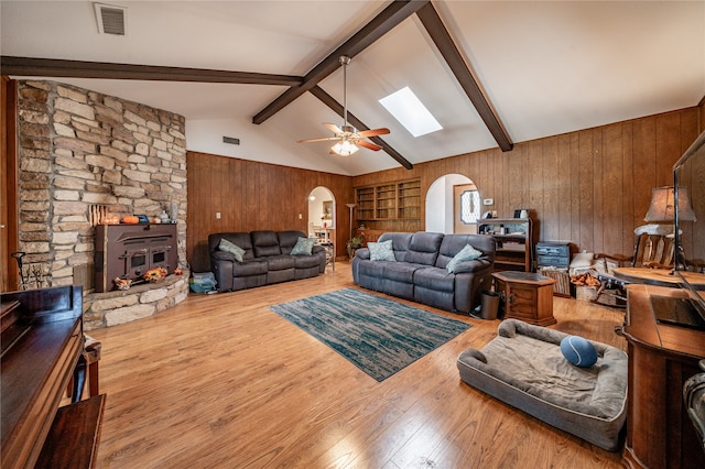 living room with ceiling fan, hardwood / wood-style flooring, vaulted ceiling with skylight, and wooden walls