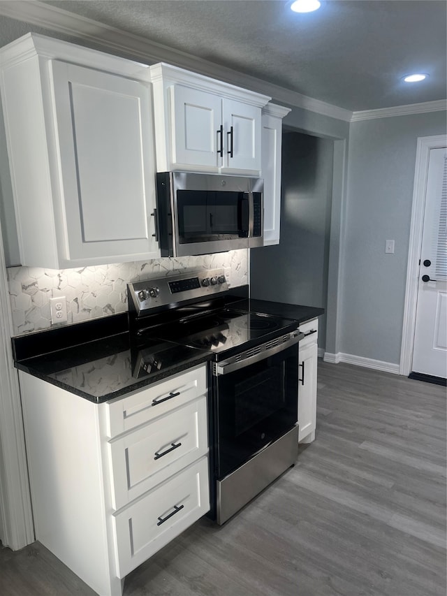 kitchen featuring ornamental molding, light hardwood / wood-style floors, stainless steel appliances, white cabinets, and decorative backsplash