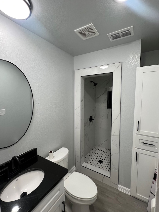 bathroom with tiled shower, toilet, wood-type flooring, vanity, and a textured ceiling