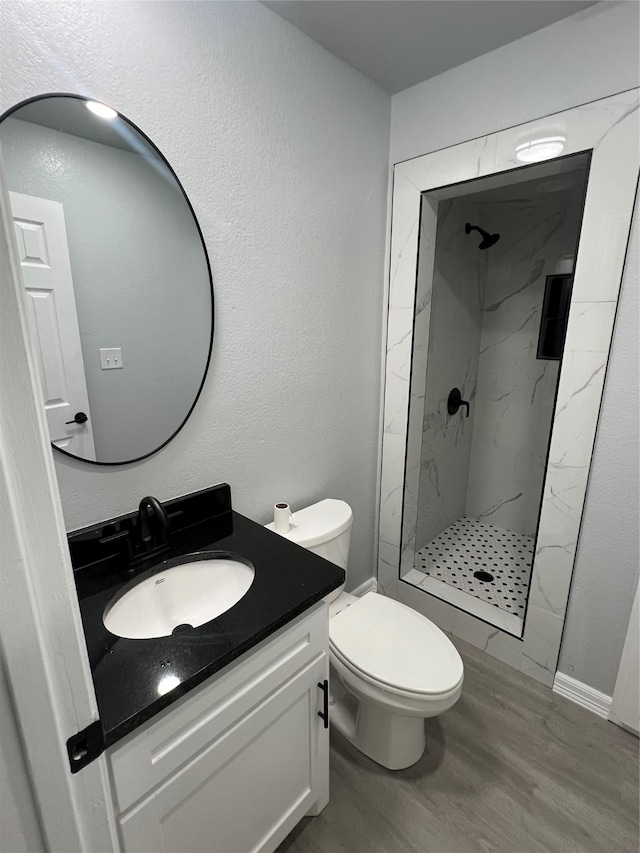 bathroom with vanity, toilet, wood-type flooring, and tiled shower