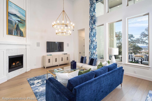 living room featuring a fireplace, a towering ceiling, a chandelier, and light wood-type flooring