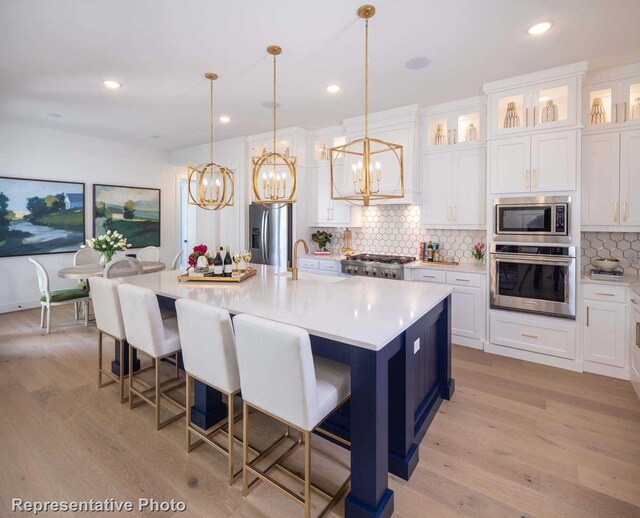 kitchen with a spacious island, stainless steel appliances, decorative light fixtures, and light hardwood / wood-style floors