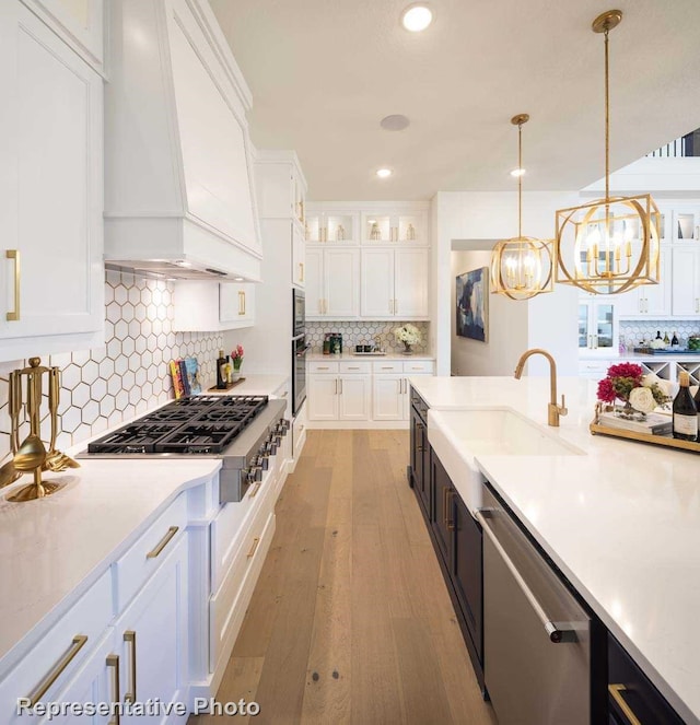 kitchen with premium range hood, white cabinets, light wood-type flooring, decorative light fixtures, and stainless steel appliances