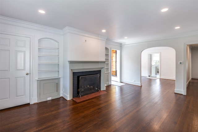 unfurnished living room featuring dark hardwood / wood-style flooring, crown molding, built in shelves, and a brick fireplace