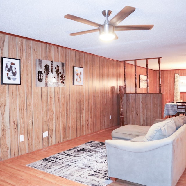 living room featuring light hardwood / wood-style flooring, wood walls, a textured ceiling, and ceiling fan