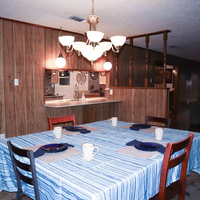 dining area featuring wood walls, a chandelier, a textured ceiling, and sink