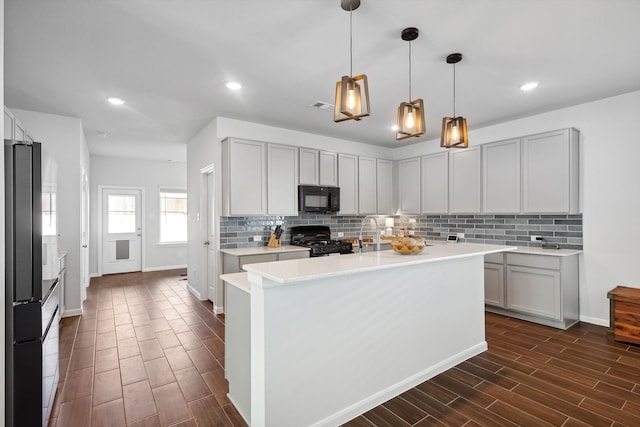 kitchen featuring hanging light fixtures, black appliances, dark hardwood / wood-style floors, and a kitchen island with sink