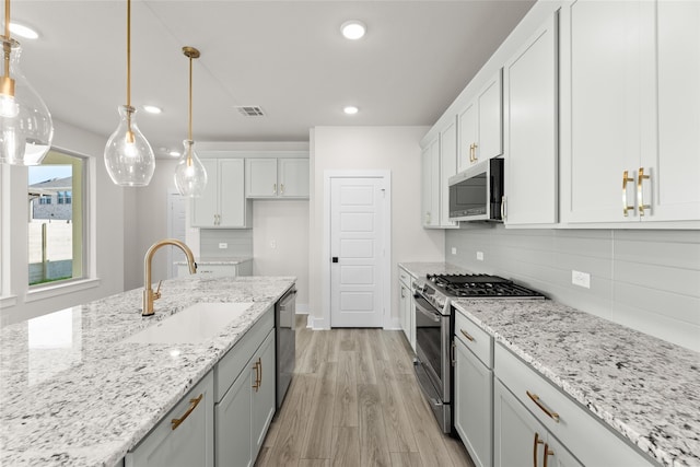 kitchen with light wood-style flooring, a sink, white cabinets, appliances with stainless steel finishes, and decorative backsplash