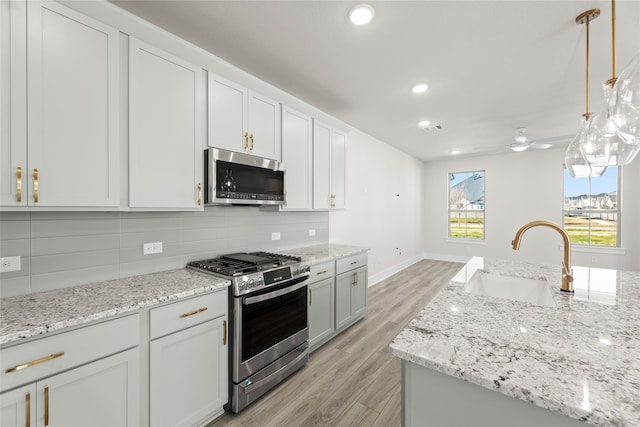 kitchen with stainless steel appliances, tasteful backsplash, light wood-style flooring, ceiling fan, and a sink