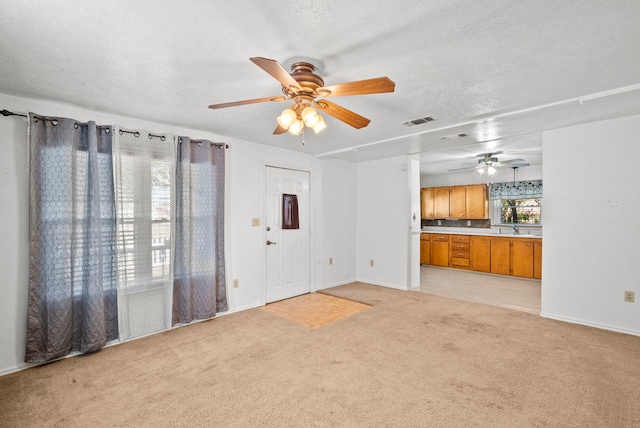 unfurnished living room with light carpet, a textured ceiling, sink, and ceiling fan