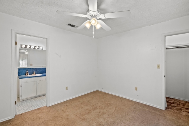 unfurnished bedroom featuring a closet, sink, light colored carpet, a textured ceiling, and ceiling fan