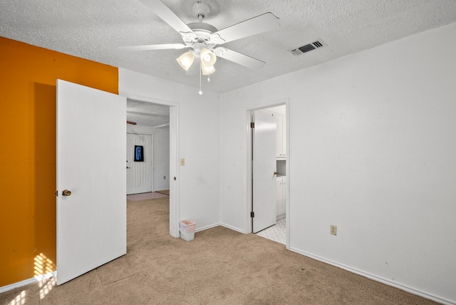 unfurnished bedroom featuring ensuite bath, a textured ceiling, light colored carpet, and ceiling fan