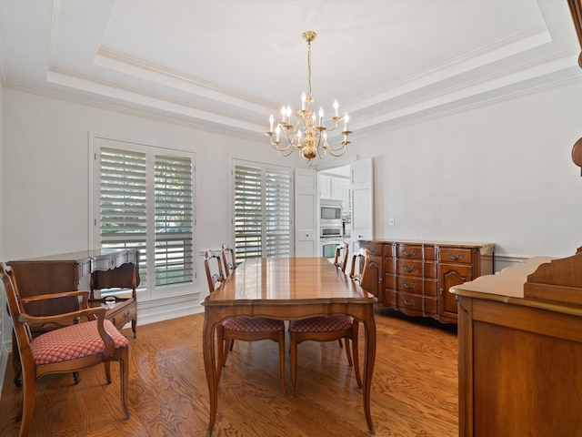 dining room with light hardwood / wood-style flooring, ornamental molding, and a tray ceiling