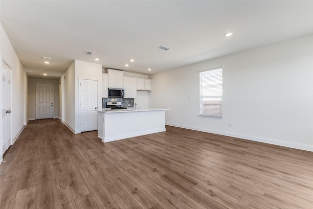 kitchen with a center island with sink, light wood-type flooring, appliances with stainless steel finishes, decorative backsplash, and white cabinets