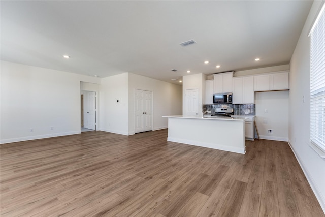 kitchen featuring white cabinetry, tasteful backsplash, an island with sink, stainless steel appliances, and light hardwood / wood-style floors