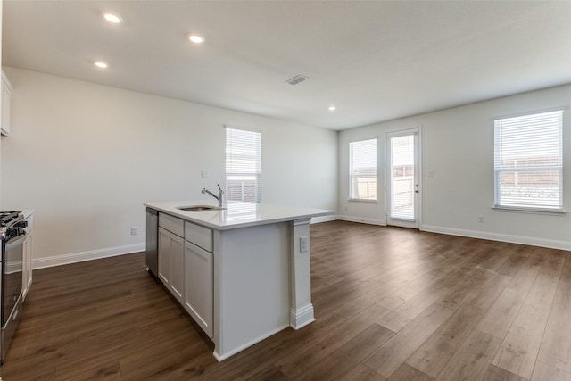 kitchen featuring an island with sink, white cabinetry, sink, stainless steel appliances, and dark wood-type flooring