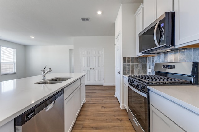 kitchen with tasteful backsplash, white cabinetry, sink, light hardwood / wood-style floors, and stainless steel appliances