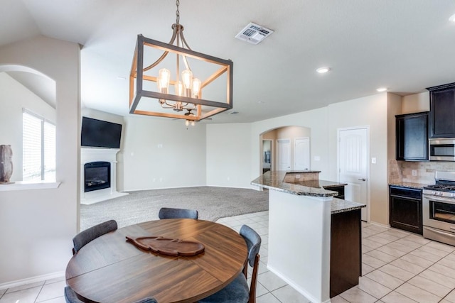 kitchen with appliances with stainless steel finishes, backsplash, a notable chandelier, light tile patterned flooring, and light stone countertops