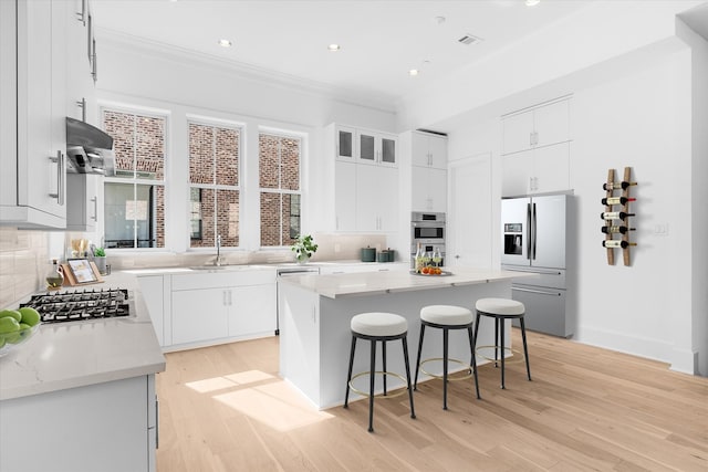 kitchen featuring white cabinets, tasteful backsplash, a kitchen island, appliances with stainless steel finishes, and light hardwood / wood-style floors