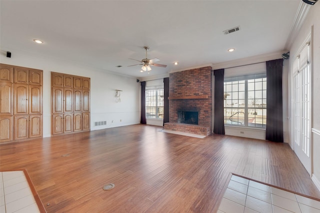 unfurnished living room featuring ceiling fan, a healthy amount of sunlight, crown molding, and a fireplace