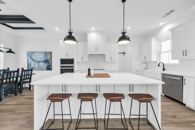 kitchen with backsplash, stainless steel appliances, white cabinets, a center island, and light hardwood / wood-style floors