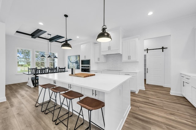 kitchen with stainless steel appliances, a kitchen island, a barn door, light hardwood / wood-style floors, and white cabinets