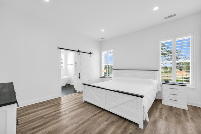 bedroom featuring wood-type flooring, a barn door, ensuite bathroom, and multiple windows