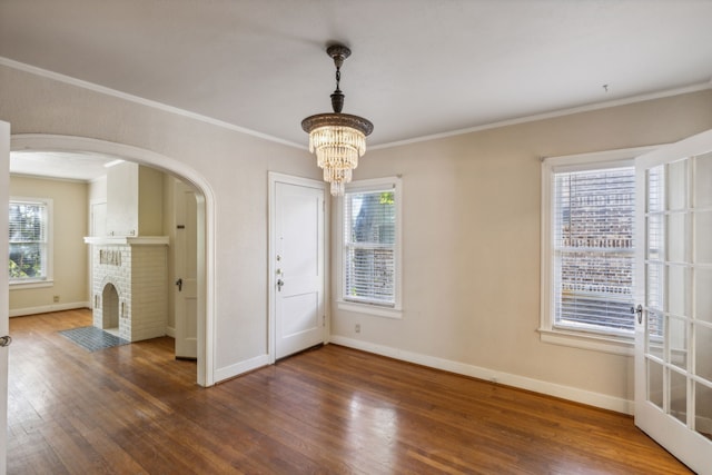 empty room with a brick fireplace, a chandelier, crown molding, and dark hardwood / wood-style flooring