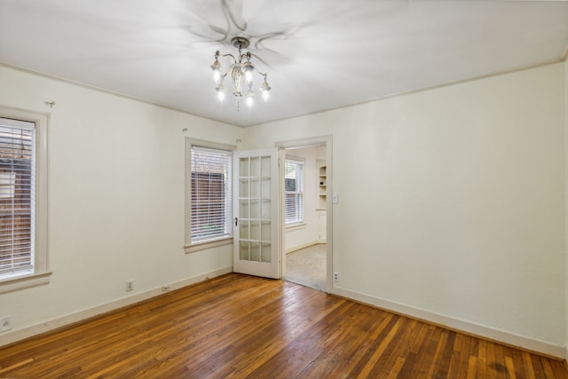 unfurnished room with a chandelier, a wealth of natural light, and dark hardwood / wood-style flooring