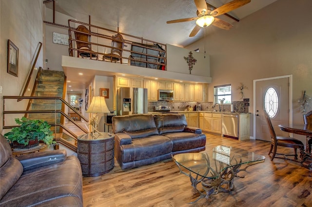 living room with sink, light wood-type flooring, high vaulted ceiling, and ceiling fan