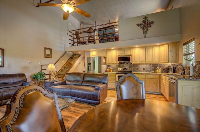 kitchen with stainless steel appliances, sink, light wood-type flooring, high vaulted ceiling, and ceiling fan