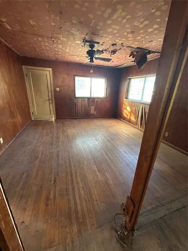 spare room with ceiling fan, wood-type flooring, and wood walls