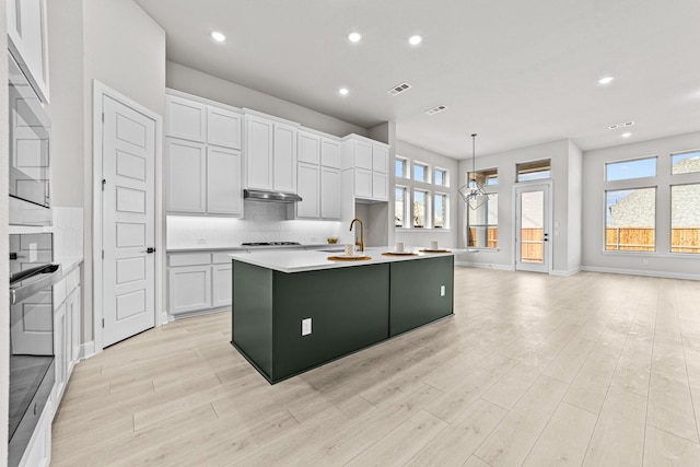 kitchen featuring decorative light fixtures, white cabinetry, sink, backsplash, and a kitchen island with sink