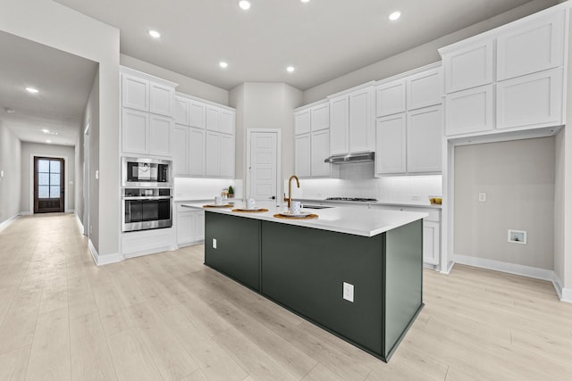 kitchen with white cabinetry, stainless steel appliances, light hardwood / wood-style floors, and an island with sink