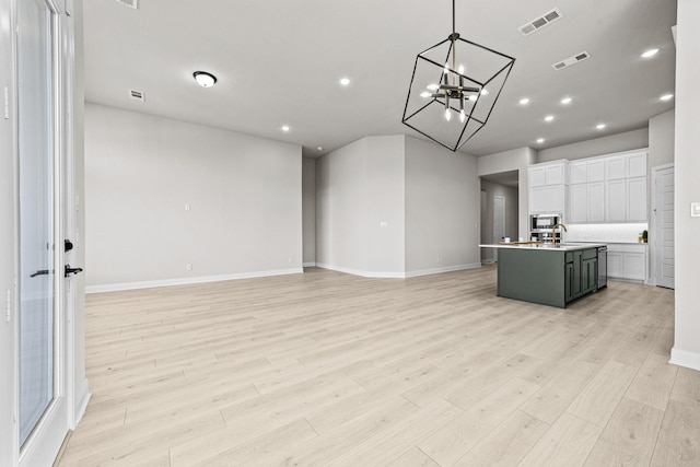 interior space with decorative light fixtures, white cabinets, backsplash, a center island with sink, and light hardwood / wood-style flooring