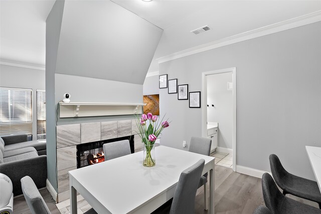 dining space featuring light hardwood / wood-style flooring, crown molding, vaulted ceiling, and a tile fireplace