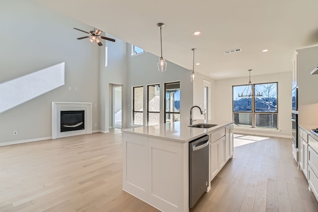 kitchen with a center island with sink, white cabinets, sink, light hardwood / wood-style flooring, and decorative light fixtures