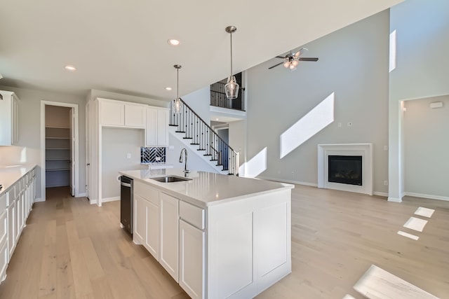 kitchen with sink, pendant lighting, white cabinets, light hardwood / wood-style floors, and an island with sink