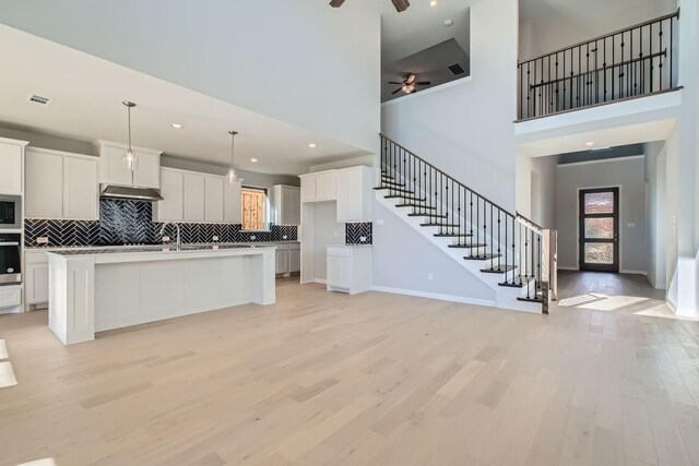 kitchen featuring a high ceiling, light hardwood / wood-style floors, white cabinetry, and an island with sink