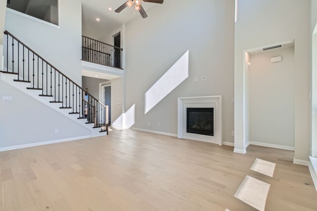 unfurnished living room featuring ceiling fan, a towering ceiling, and light hardwood / wood-style flooring