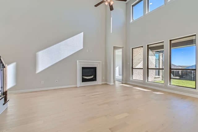 unfurnished living room with ceiling fan, a towering ceiling, and light wood-type flooring