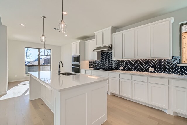 kitchen with a kitchen island with sink, hanging light fixtures, sink, light hardwood / wood-style flooring, and stainless steel appliances