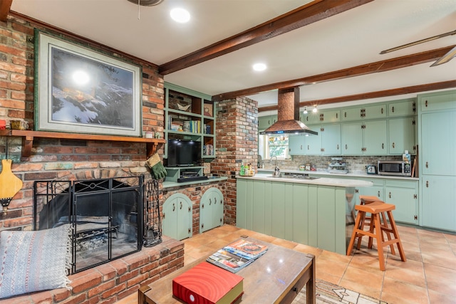 kitchen with a brick fireplace, island range hood, kitchen peninsula, green cabinets, and beamed ceiling