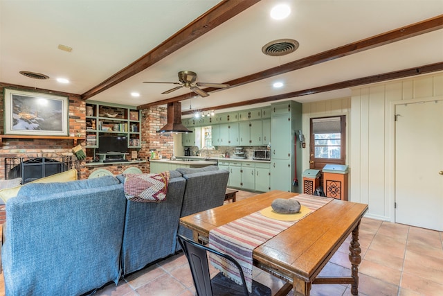 dining room featuring a brick fireplace, beamed ceiling, ceiling fan, and light tile patterned flooring