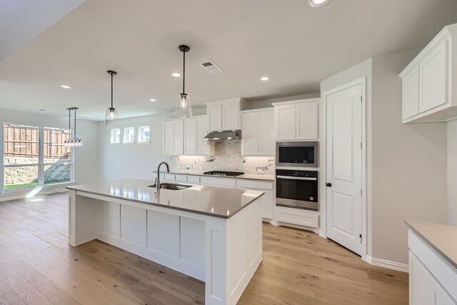 kitchen featuring built in microwave, oven, hanging light fixtures, a kitchen island with sink, and black gas stovetop