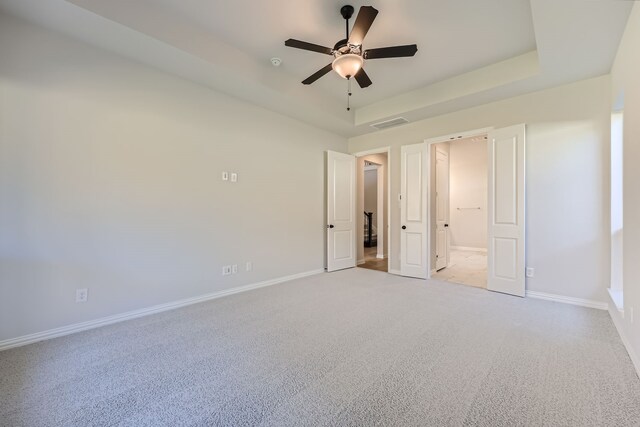 unfurnished bedroom featuring a tray ceiling, light colored carpet, and ceiling fan